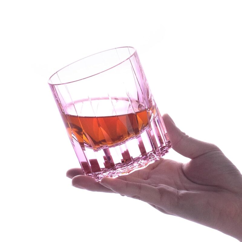 Pink KAMMAK crystal whiskey glass held in hand with an amber pour
