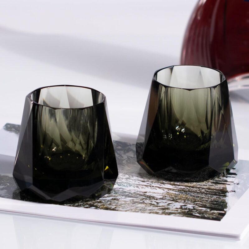 Two smoky faceted KAMMAK whiskey glasses styled on a reflective home-bar surface