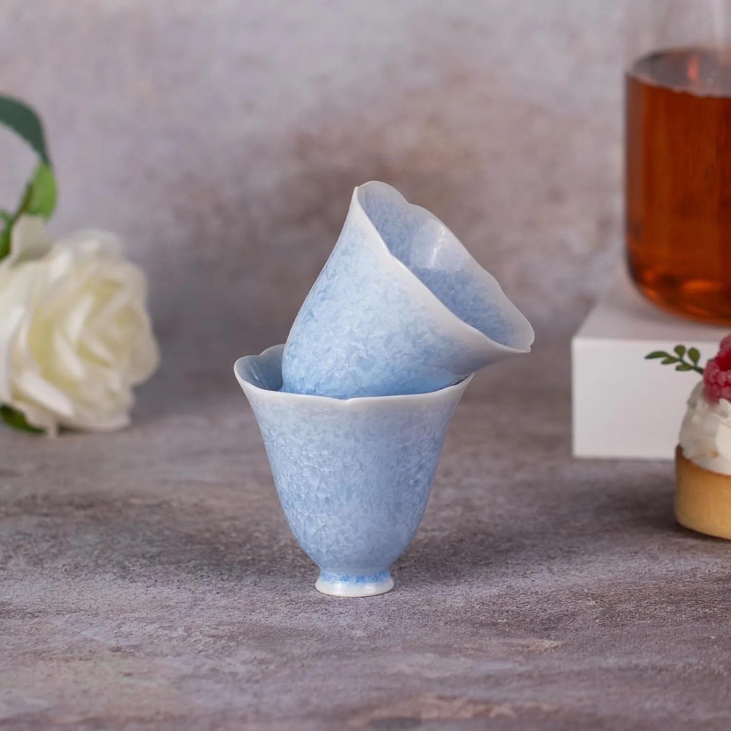 Stacked blue petal-rim tea cups beside a tea setting