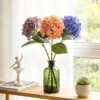 Colorful hydrangea stems arranged in a tall green glass bottle KAMMAK 8KPFZH004 home decor product styled home decor setting image 5