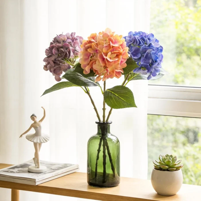 Colorful hydrangea stems arranged in a tall green glass bottle KAMMAK 8KPFZH004 home decor product styled home decor setting image 5