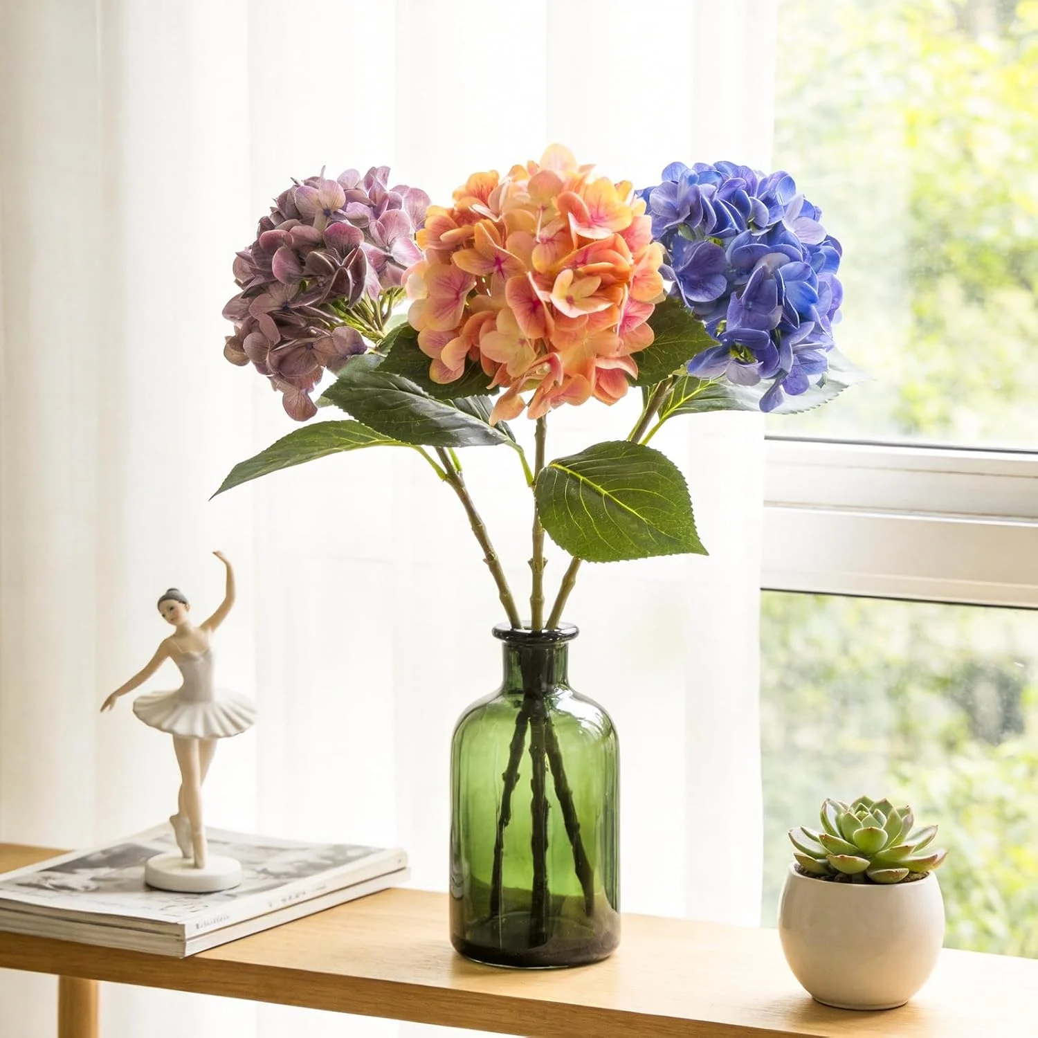 Colorful hydrangea stems arranged in a tall green glass bottle