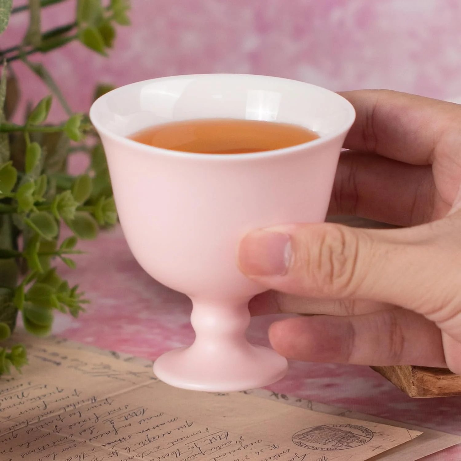 Blush pink pedestal tea cup held with tea inside