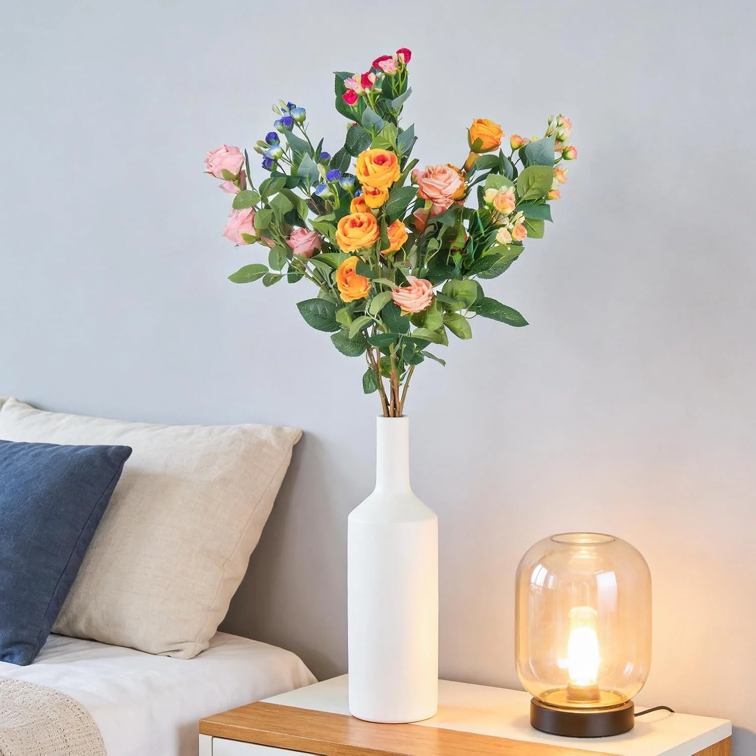 Bright artificial rose arrangement in a white vase by a sofa
