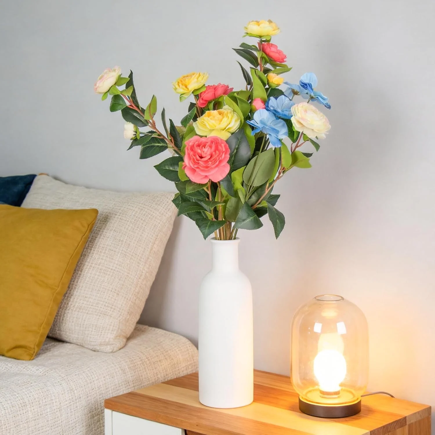 Colorful artificial roses in a white vase beside a sofa
