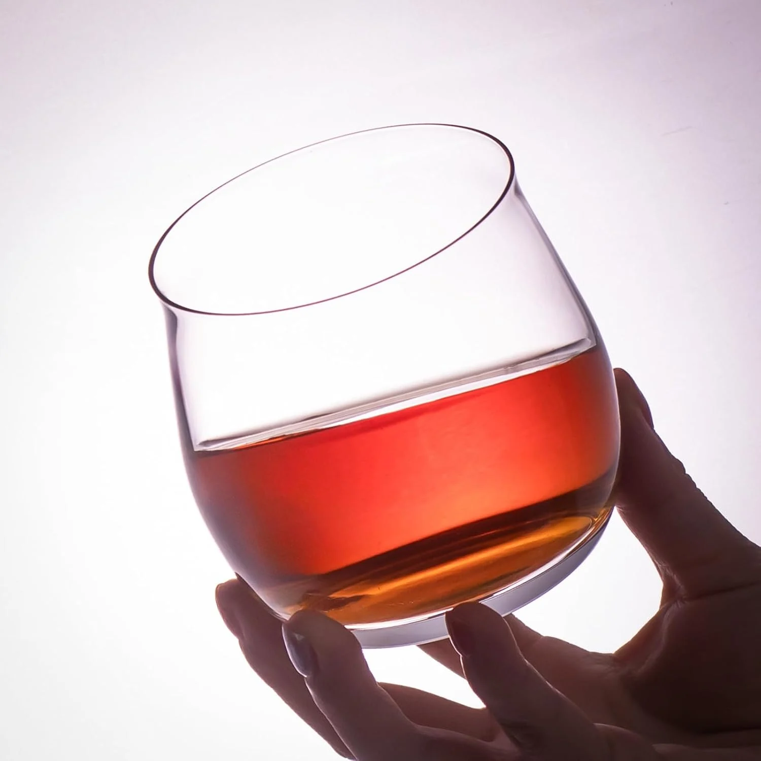 Rounded crystal whiskey glass held at an angle with a red drink