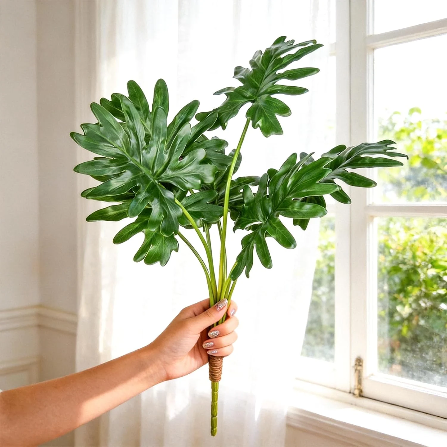 Artificial split-leaf greenery bundle held near a window