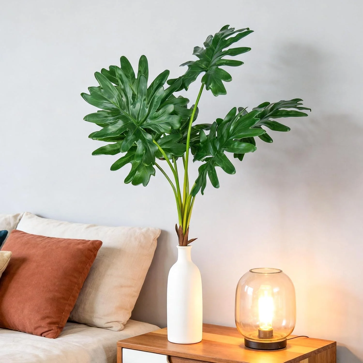 Artificial tropical-style leaves in a white vase beside a sofa