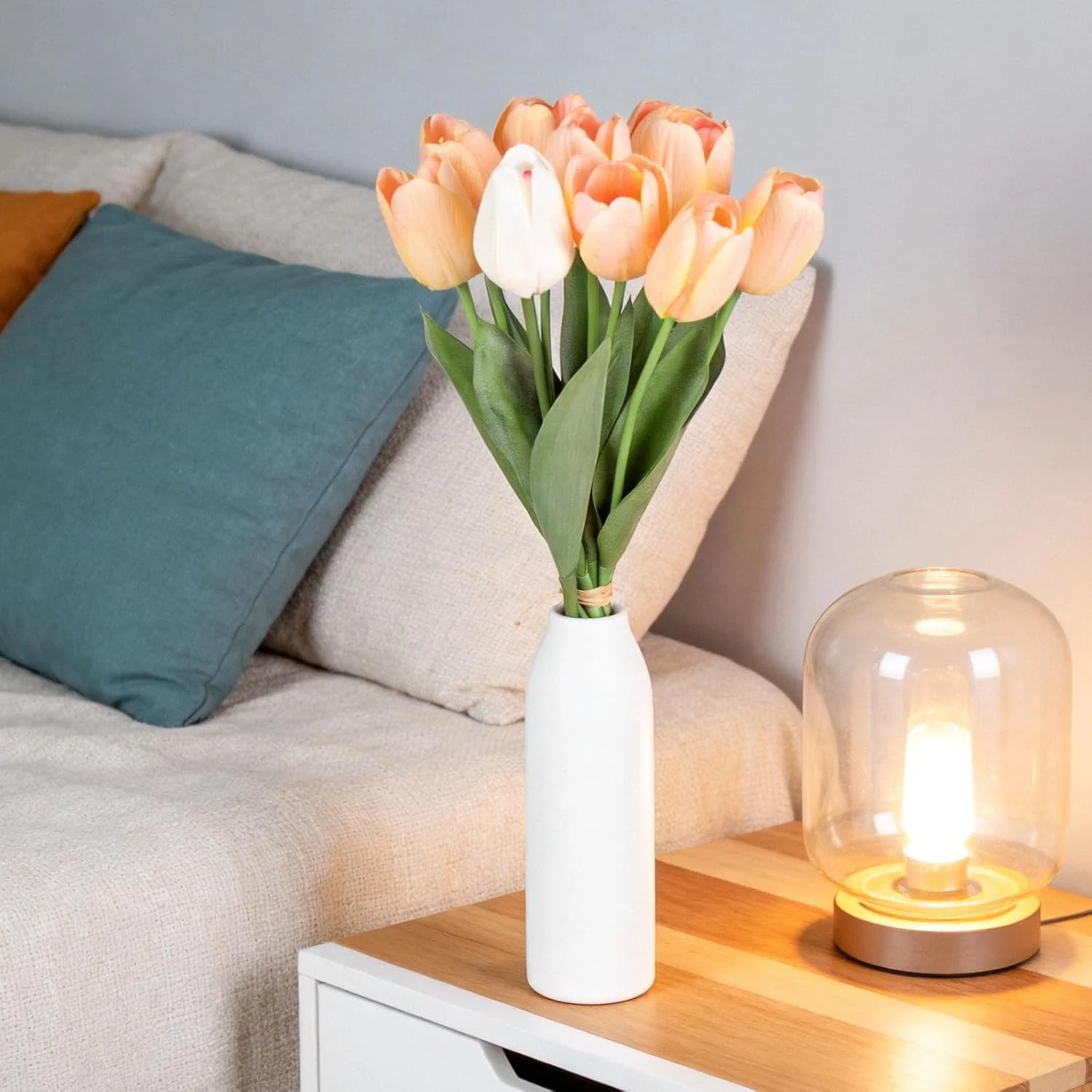 Artificial tulips displayed in a white vase beside a sofa