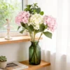Blush hydrangea stems arranged in a green bottle on a shelf KAMMAK 8KPFZH006 home decor product styled home decor setting image 5