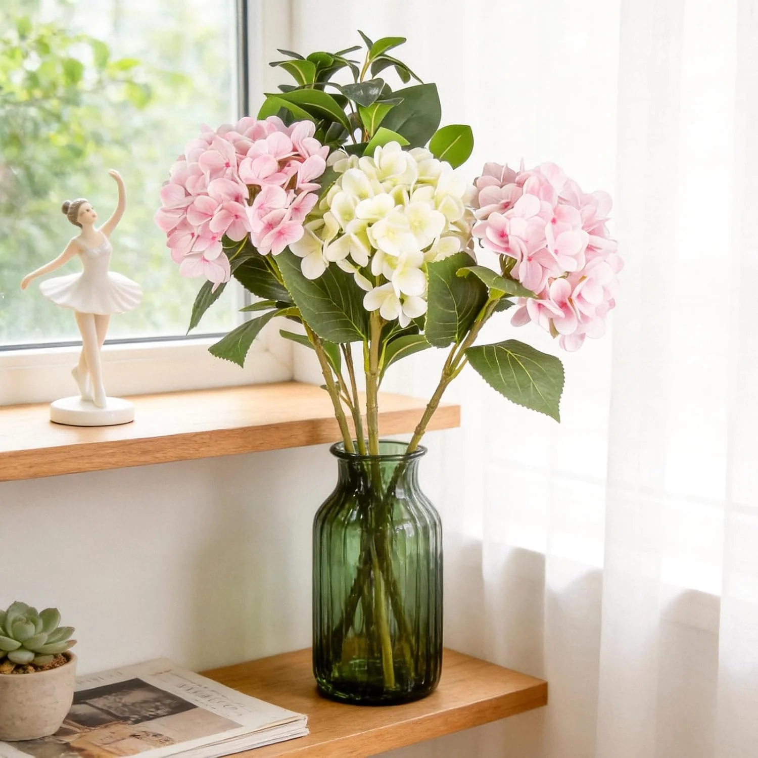 Blush hydrangea stems arranged in a green bottle on a shelf