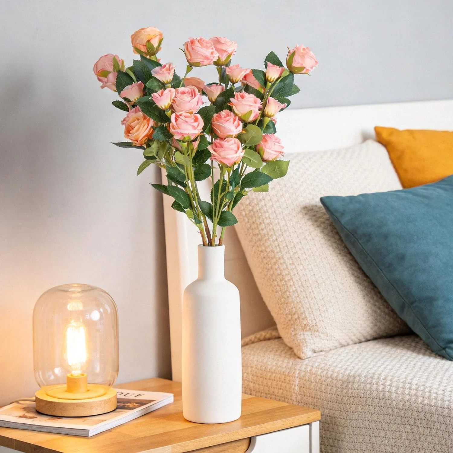Blush artificial roses displayed in a white vase by a sofa