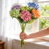Multicolor hydrangea bouquet held beside a sunlit window KAMMAK 8KPFZH009 home decor product side angle view showing silhouette