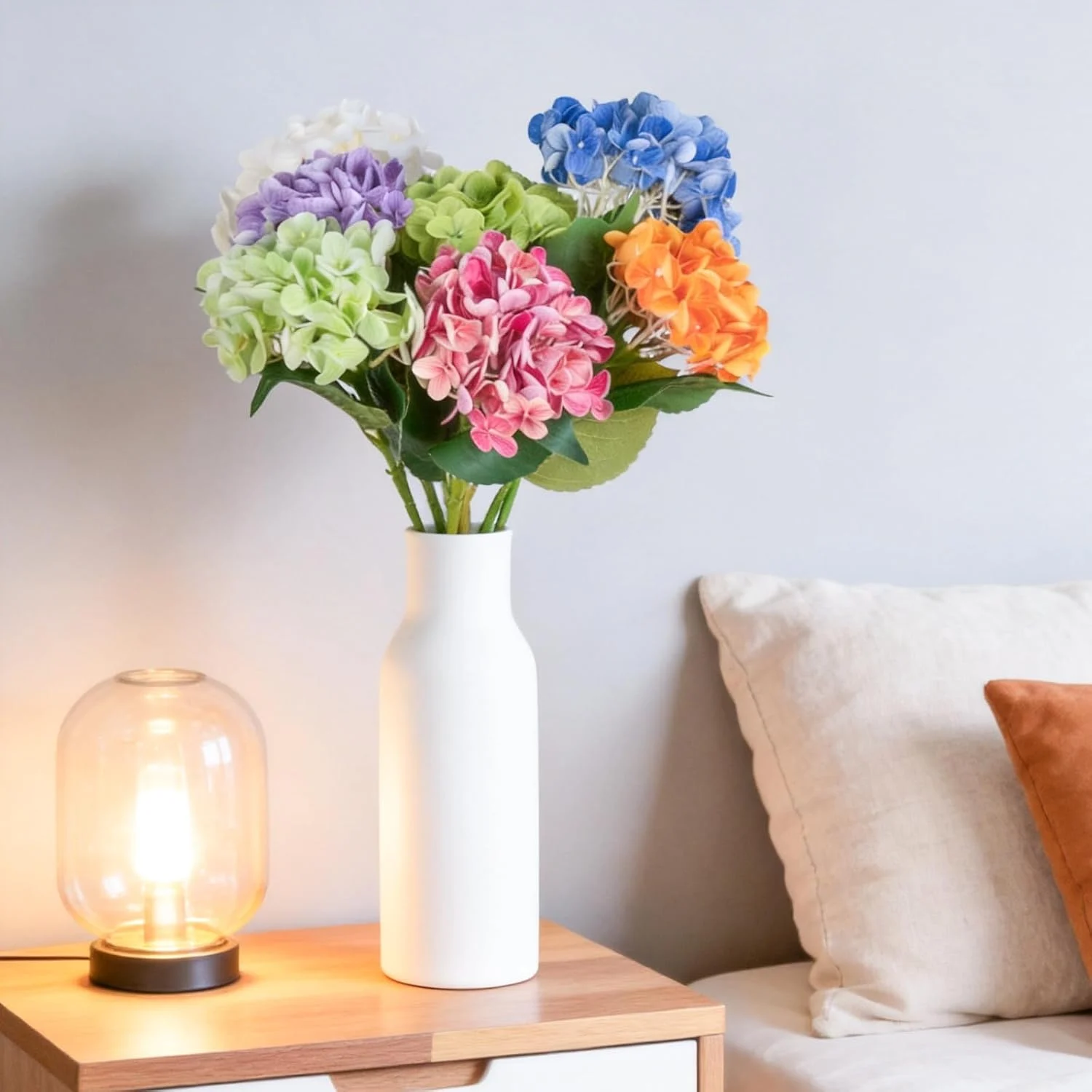 Bright mixed hydrangeas in a white vase beside a sofa
