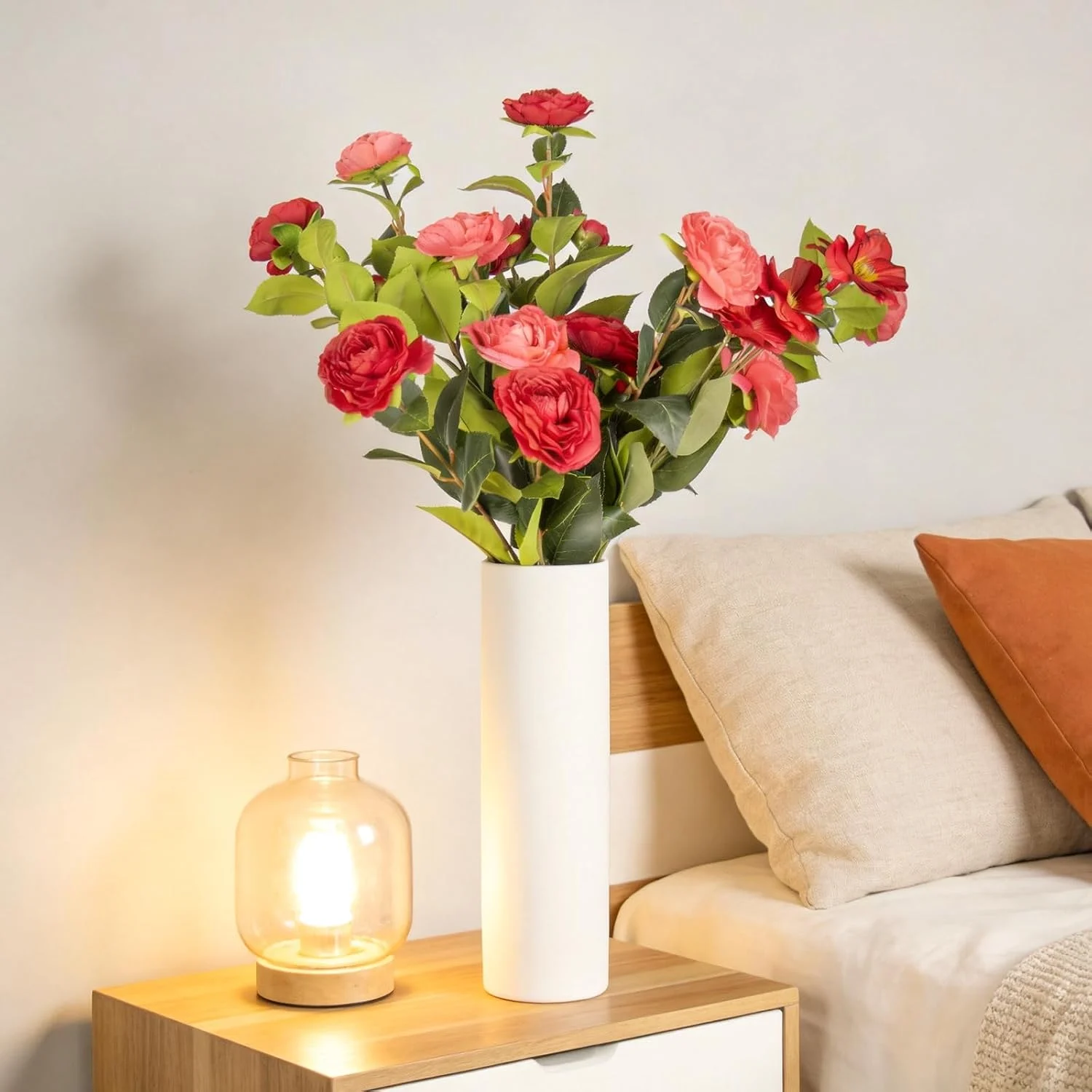 Red mixed flowers displayed in a white vase beside a sofa