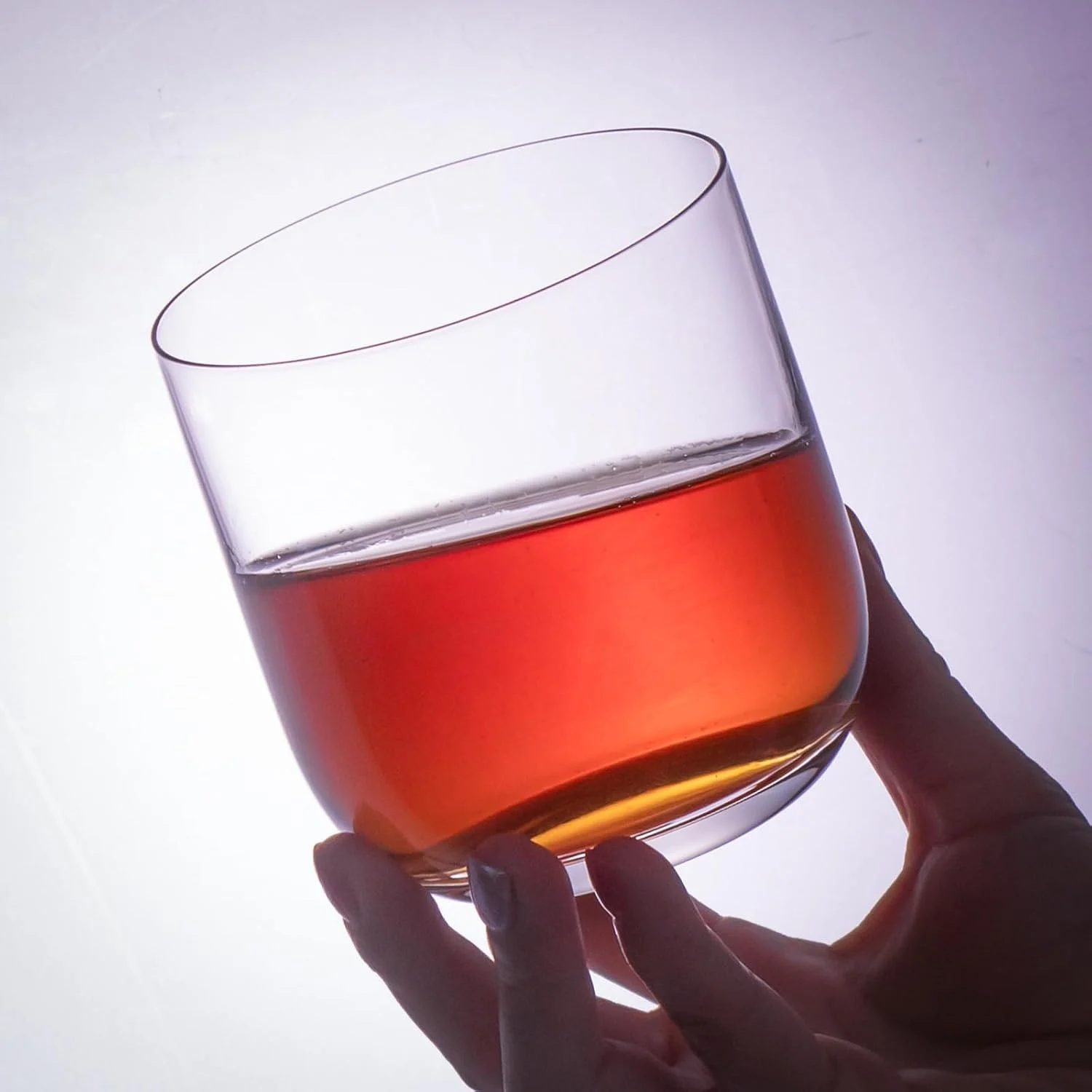 Straight crystal whiskey glass held up with an amber drink