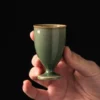 Single olive green KAMMAK footed tea cup held against a dark background KAMMAK 7KPSP694N+695N ceramic cup and saucer shape and proportion detail image 3