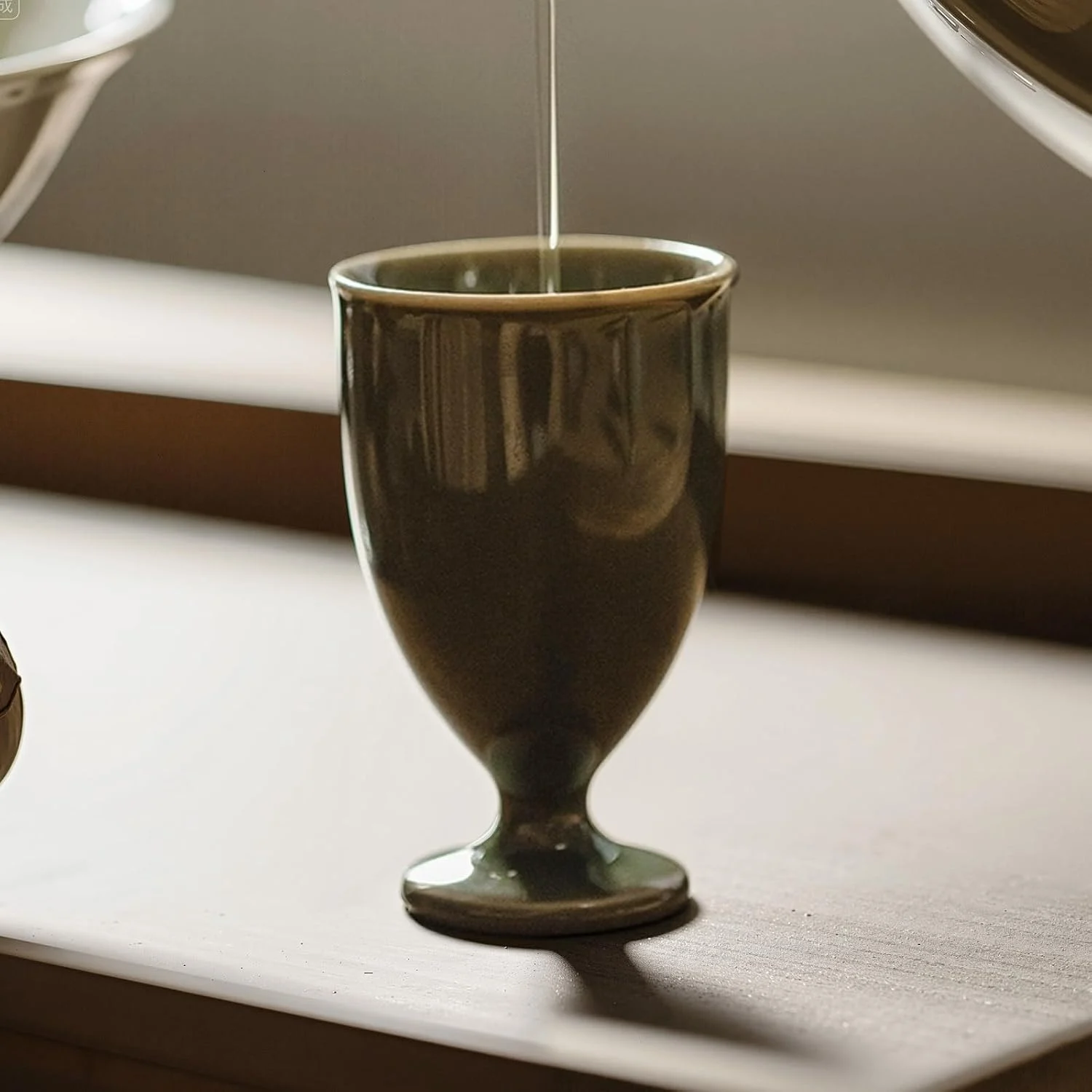 Tea being poured into an olive green KAMMAK high-footed cup