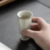 Single pale green KAMMAK 718N footed tea cup held above a table KAMMAK 7KPSP718N ceramic cup and saucer shape and proportion detail image 3