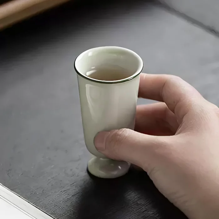 Single pale green KAMMAK 718N footed tea cup held above a table KAMMAK 7KPSP718N ceramic cup and saucer shape and proportion detail image 3