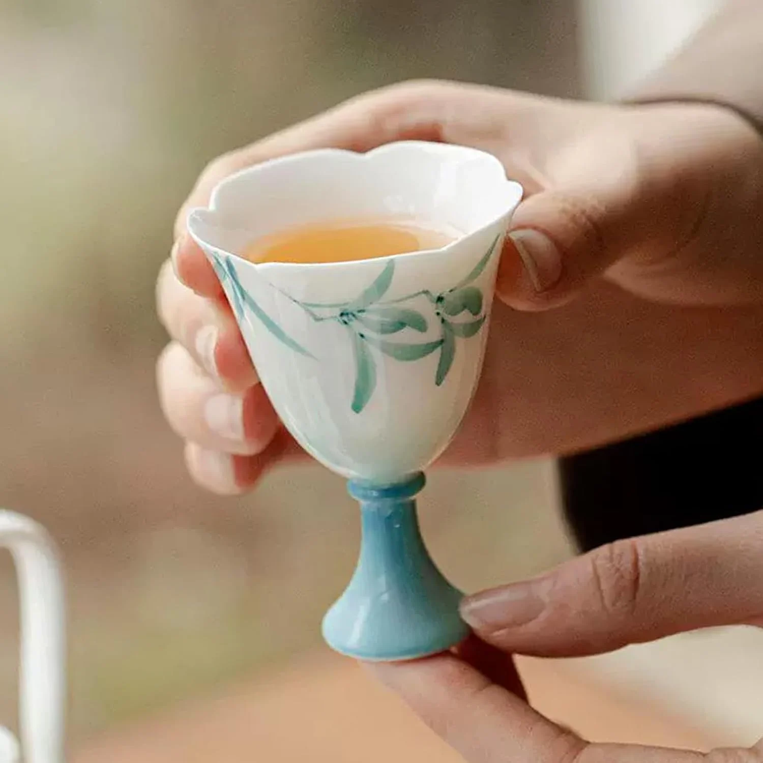 Teal KAMMAK floral footed tea cup held with tea inside