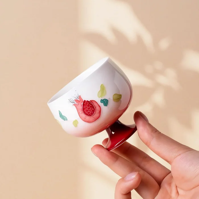 KAMMAK pomegranate ceramic tea cup balanced on its glossy red foot KAMMAK 7KPSP698N ceramic cup and saucer styled home decor setting image 5