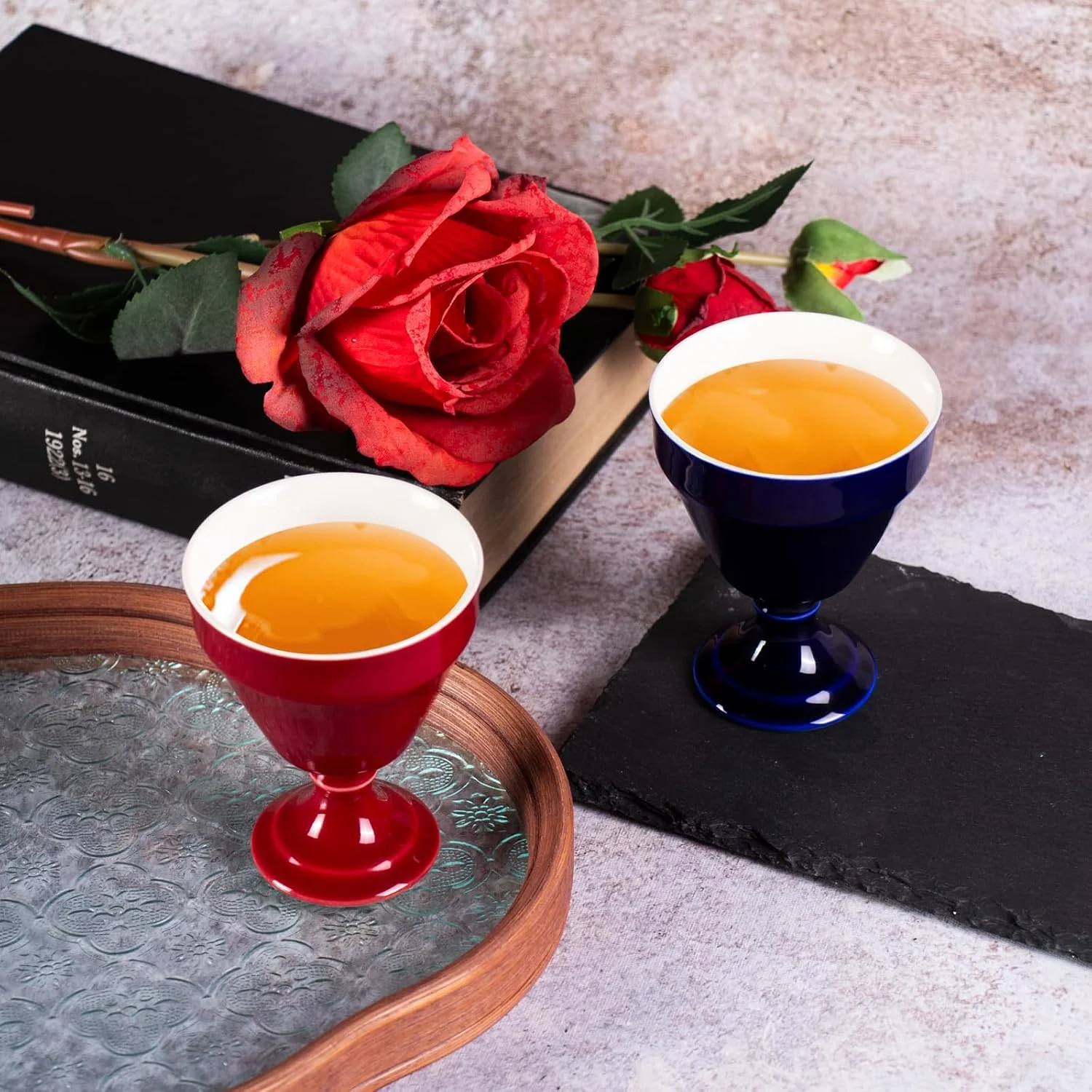 Red and navy KAMMAK footed cups filled with tea beside roses